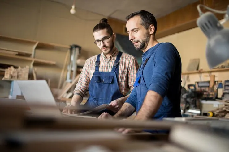 Two small business owners reviewing invoices on a laptop in their workshop